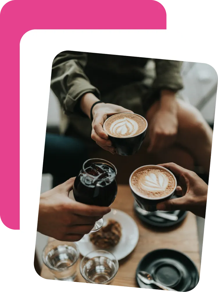 Three people raising coffees and a cold brew over a café table
